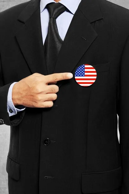 Close-up shot of the hands of two diplomats, one American and one from a Middle Eastern country, shaking hands firmly over a table with documents. The focus is on the hands and the sense of agreement and collaboration.