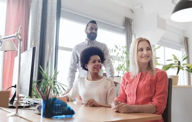 A diverse group of people working together in an office setting, with a focus on a computer screen displaying the E-Verify system and the words