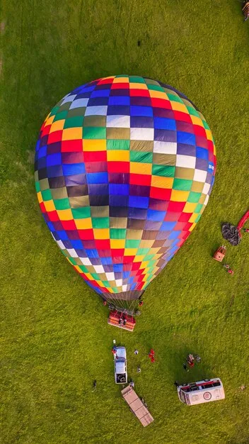 A mass ascension of hundreds of colorful hot air balloons at the Albuquerque International Balloon Fiesta, filling the sky at dawn with a stunning display of shapes, colors, and light. The landscape below is a desert with scattered buildings.