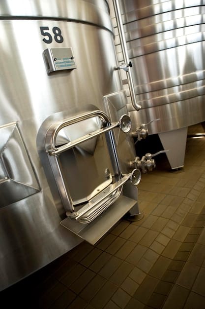 A close-up shot of brewing equipment inside a microbrewery. Highlight the stainless steel tanks, pipes, and gauges, conveying the technical and hands-on nature of craft brewing. Include a brewer in the background, checking the equipment, to add a human element.