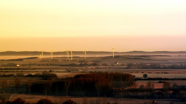 A wind farm at sunset, with solar panels visible in the distance, symbolizing renewable energy and sustainable business practices.